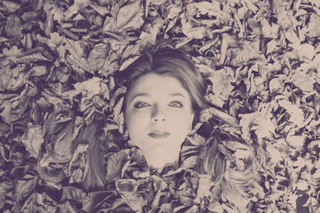 Art symbolism nature outdoor fun concept. Young ginger covered by leaves. Redhead girl drowning in...