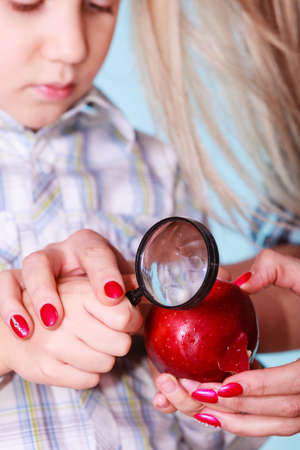 Early education nature and biology. Mother help son examine fruit apple with magnifying glass. Teacher help discover environment.の写真素材