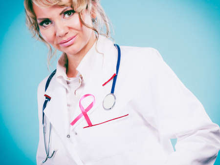 Breast cancer. Medical help treatment concept. Female blonde doctor in white medic apron with pink ribbon on blue background.の写真素材
