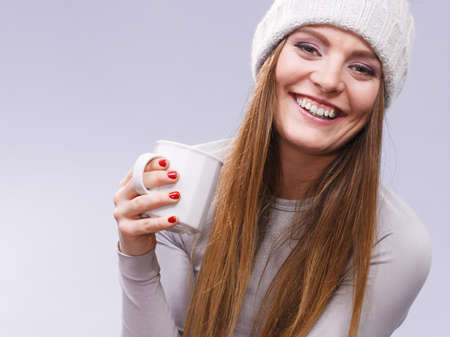 Attractive woman long hair girl in winter wool cap holds mug with tea hot beverage, warming herself...