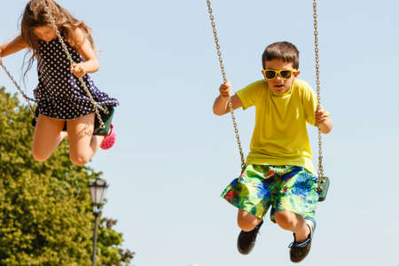 Fun and joy of children. Little girl and boy playing outdoor on preschool playground garden. Kids swinging on swing-set to touch the sky.の写真素材