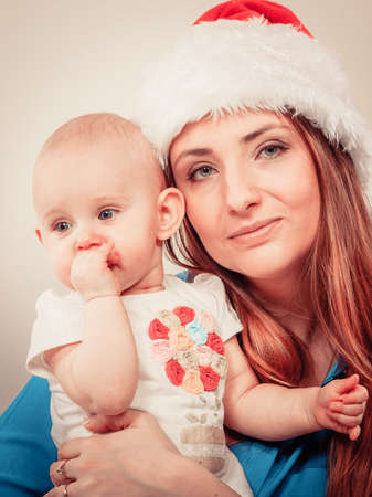 Family celebration concept. Christmas woman with cute baby. Beautiful lady has red santa claus cap.の写真素材