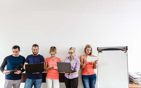 Education social media concept. Male and female diversity students young people studying using computer tablet smartphone, standing on wall with copy spaceの写真素材