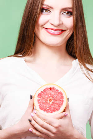 Woman attractive long hair girl holding half of grapefruit citrus fruit in hand. Healthy diet food. Summer vacation holidays concept. Studio shot on greenの写真素材
