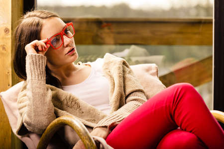 Woman wearing red glasses sitting at home on rocker chair in front of window in her living room relaxingの写真素材