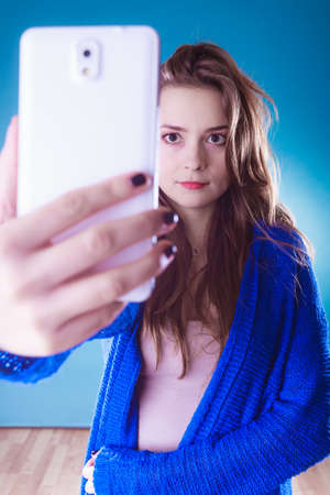 Young woman nowadays. Using phone to take selfie. Pretty girl in sweater.