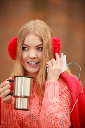 Autumn season time people concept. Young woman holding thermal mug. Cold weather outside. Lady has red clothing.の写真素材