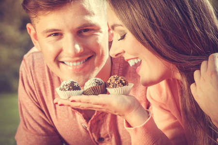 Love and dating. Attractive woman giving cupcakes cookies to handsome man. Happy cute lovers on date outdoor.の写真素材