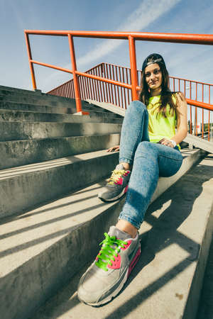 Cool young long haired girl sitting on the urban stairs. Active lifestyle funky in summer. Trendy sport teen.の写真素材
