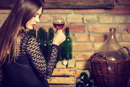 Elegant beauty lady long hair full make up wearing black dress tasting wine in rural cottage interior cellerの写真素材