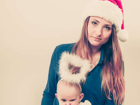 Family celebration concept. Christmas woman with cute baby. Beautiful lady has red santa claus cap.の写真素材