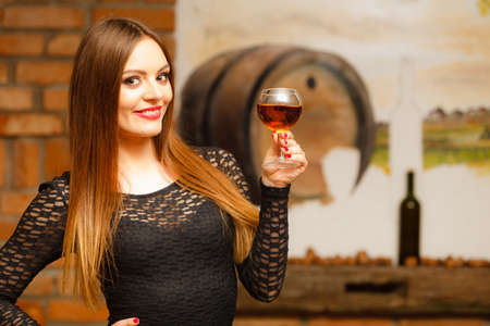 Elegant beauty lady long hair full make up wearing black dress tasting wine in rural cottage interior cellerの写真素材