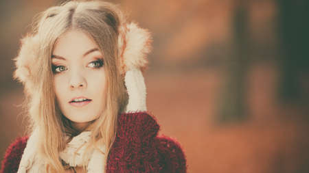 Portrait of pretty attractive fashionable woman in fall forest park. Gorgeous young girl in earmuffs and maroon sweater pullover. Autumn winter fashion.の写真素材