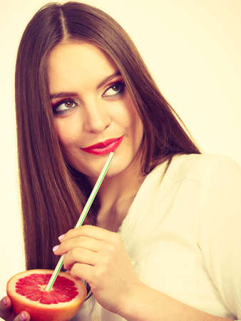 Woman attractive long hair girl eyes makeup holding grapefruit citrus sipping juice from fruit. Healthy diet food. Summer vacation holidays concept. Toned imageの写真素材