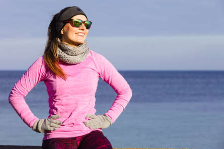 Woman resting relaxing after doing sports outdoors. Fitness girl female jogger wearing warm sporty clothes in cold day weather on seaside taking breakの写真素材