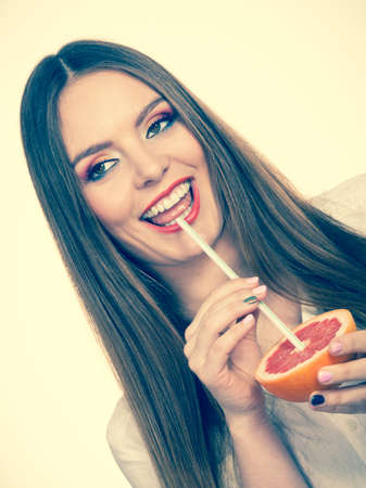 Woman attractive long hair girl eyes makeup holding grapefruit citrus sipping juice from fruit. Healthy diet food. Summer vacation holidays concept. Toned imageの写真素材