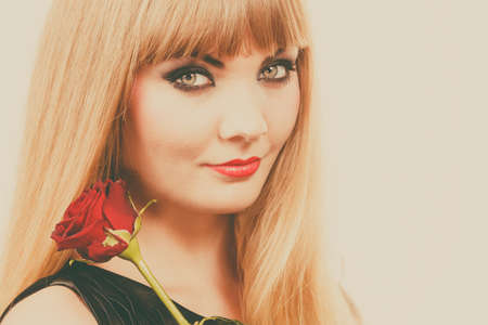 Woman holding rose flower. Attractive blonde lady dark makeup studio shot toned image. Beauty, holidays, celebration conceptの写真素材