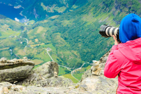 Tourism vacation and travel. Female tourist taking photo with camera, enjoying Geiranger fjord and mountains landscape from Dalsnibba Plateau viewpoint, Norway Scandinavia.の写真素材