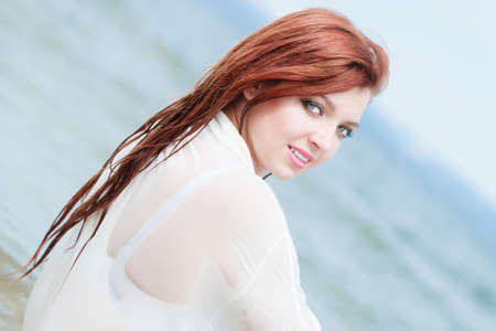 Vacation. Sensual girl wet cloth in water on the coast. Redhair woman having fun relaxing on the sea. Summertime.の写真素材