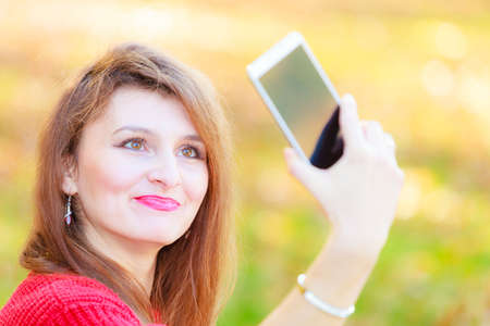 Nature outdoor technology social concept. Gorgeous girl taking selfie. Young lady in park takes picture of herself amidst autumnal vegetation.の写真素材