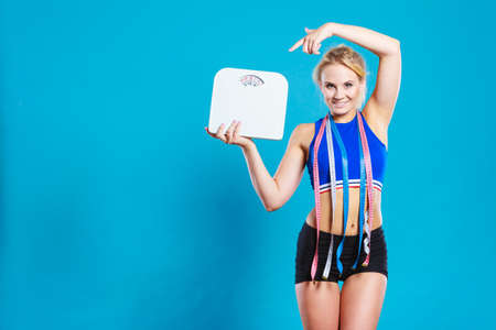 Healthy lifestyle. Fitness woman with many measure tapes holding weight scale studio shot blue backgroundの写真素材