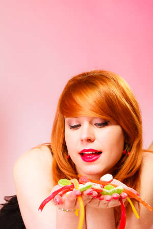 Candy addiction. Multi colored jelly sweets in red haired woman hands. Studio shot.の写真素材