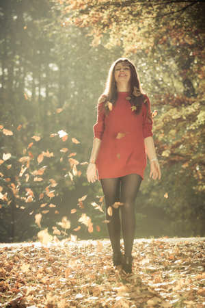 Joy and freedom. Young enjoyable attractive woman having fun with autumnal leaves float in the air in park. Playful girl relaxing outdoor.の写真素材