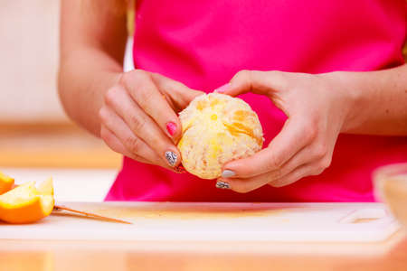 Woman young housewife in kitchen at home peeling orange fruit for salad or juicing. Healthy eating, cooking, raw food, dieting and people concept.の写真素材