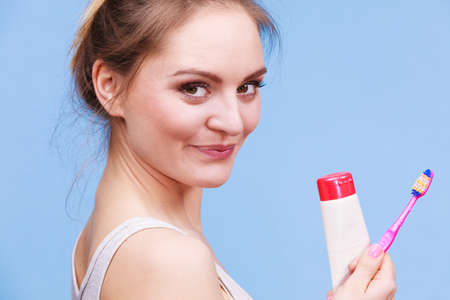 Woman holding brush and tooth paste for teeth cleaning. Happy smiling girl with toothbrush. Oral hygiene. Studio shot blue backgroundの写真素材