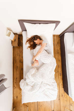 Mornings people concept. Sleepy woman sleeping in the bed. Attractive lady changing sleep positions.の写真素材