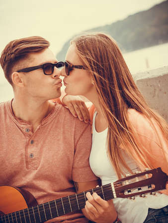 Instruments and musical concept. Young happy kissing couple with instrument man playing classic guitar dating outdoor at sea.の写真素材