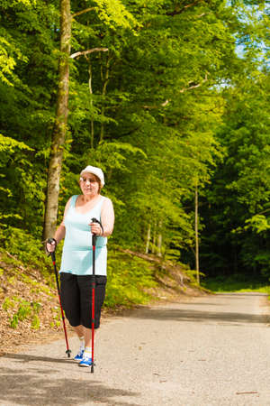 Healthy active retirement concept. Senior woman practicing nordic walking in forest park. Elderly female enjoying nature fresh airの写真素材