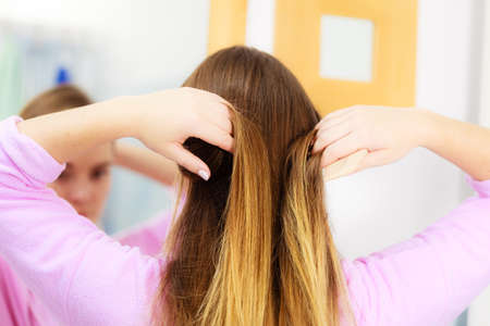 Woman combing brushing her long smooth hair in bathroom, looking in mirror. Girl taking care refreshing her hairstyle. Haircare concept.の写真素材