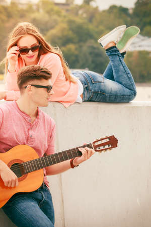 Instruments and musical concept. Young happy couple with instrument man playing classic guitar dating outdoor at sea.の写真素材