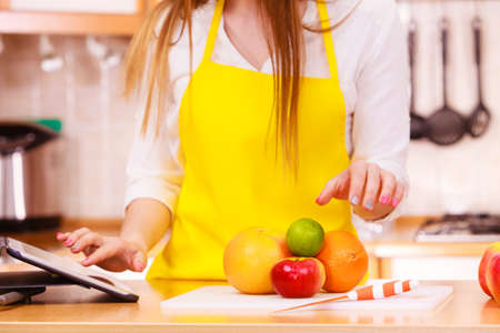 Woman young housewife in kitchen with many fruits on counter using tablet looking at recipes. Healthy eating, cooking, vegetarian food, dieting and technology concept.の写真素材