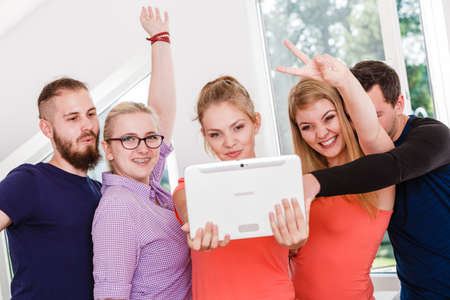 Fun bonding selfie concept. Group of diverse friends students classmates taking self photo with tablet pc computer indoors in classの写真素材