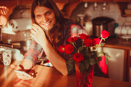 Waiting for love concept. Date time. Happy young smilin man with smartphone mobile phone and bouquet...