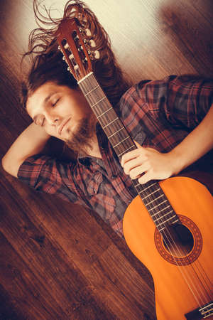 Sleeping man with guitar. Lying on the floor and enjoying the moment.