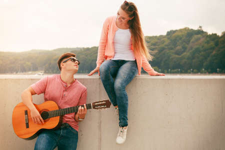 Instruments and musical concept. Young happy couple with instrument man playing classic guitar dating outdoor at sea.の写真素材