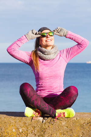 Woman resting relaxing after doing sports outdoors. Fitness girl female jogger wearing warm sporty clothes in cold day weather on seaside taking breakの写真素材