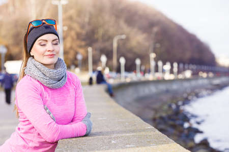 Woman resting relaxing after doing sports outdoors. Fitness girl female jogger wearing warm sporty clothes in cold day weather on seaside taking breakの写真素材
