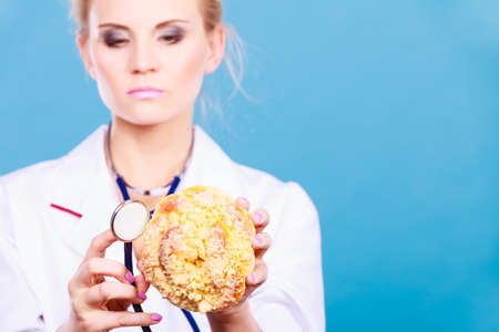 Serious dietitian nutritionist checking examine sweet roll bun with stethoscope. Woman with...