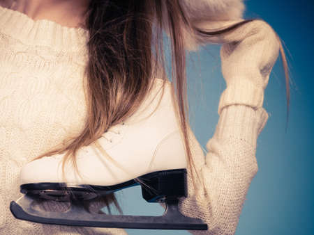 Woman carrying a pair of ice skates getting ready for ice skating, winter sport activity, on blueの写真素材
