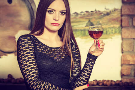 Elegant beauty lady long hair full make up wearing black dress tasting wine in rural cottage interior cellerの写真素材
