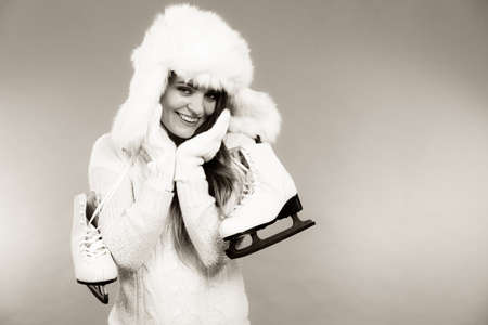 Winter sports clothing concept. Attractive lady with ice skate. Young woman wearing white cozy outfit.の写真素材