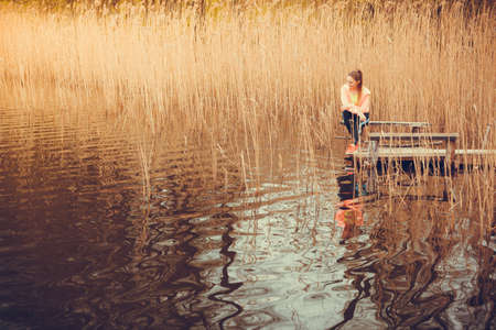 Sport and lifestyle concept. Young sports woman female jogger taking break from run workout, relaxing on wooden bridge, water and reed aroundの写真素材