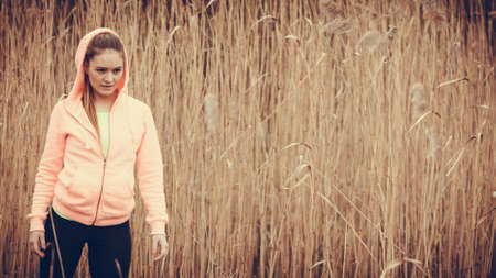 Sport and lifestyle concept. Young sports woman female jogger taking break from run workout, relaxing on wooden bridge, water and reed aroundの写真素材