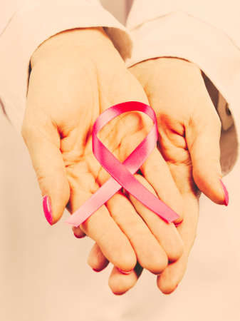 Woman doctor holding pink cancer breast ribbon in hands. Awareness of being sick. Close up. Filtered.の写真素材