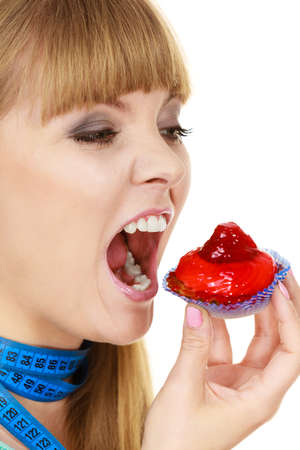 Woman undecided with blue measuring tape around her neck holds in hand cake cupcake, trying to resist temptation. Weight loss diet dilemma gluttony concept.の写真素材