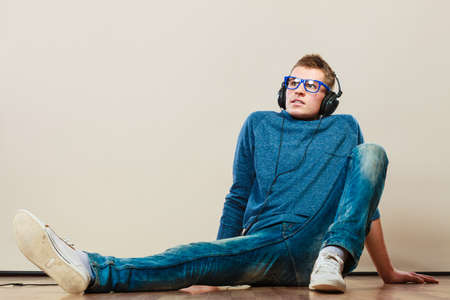 leisure and lifestyle concept. Young hipster man fashion clothes with headphones sitting on floor...